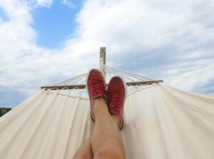 person's legs with red running shoes lying on white hammock. Daydreaming about someday