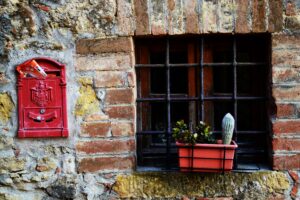 Red mail box beside window of stone house. window box with plants on window ledge