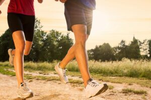 the lower legs and feet of two people running on a dirt path. Taking small steps