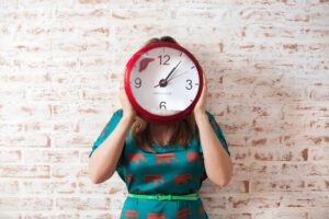 woman in green dress holding up clock over her face
