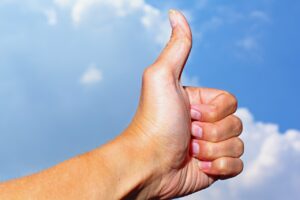 hand with thumbs up agains blue sky and white cloud