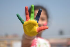 child's hand with many colours of paint showing the palm and 5 fingers