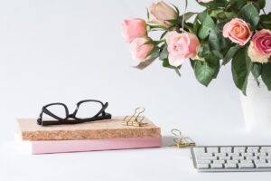 books, glasses, rose bouquet and end of keyboard on desk.