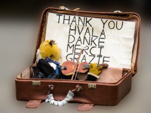 Puppet figure playing violin in briefcase with thank you, written in several languages, on a paper behind him. Getting organized can be easier using gratitude.