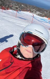 Carolyn Caldwell in skis, helmet and red ski coaching uniform at top of ski hill.