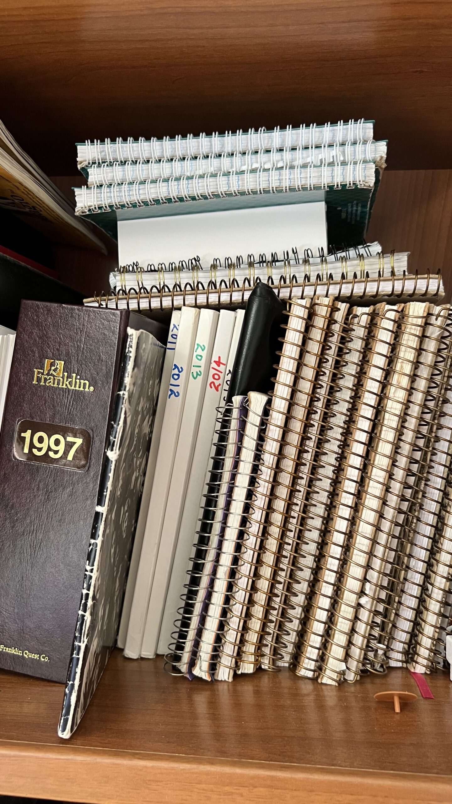 brown daytimer binder with 1997 on spine beside several spiral notebooks on shelf
