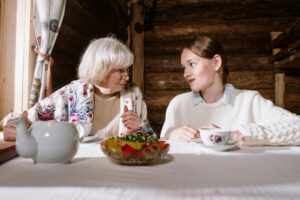 woman with grey hair drinking tea and taking to younger woman as if talking about downsizing