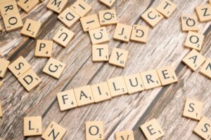 Scrabble letters spelling the word Failure on a wooden background with other random letters around