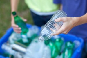 two people putting plastic bottles into a recycling bin