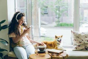 Woman with headphones looking at phone while sitting and patting dog.