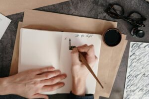 person writing "to-do list" with ink pen on in small note book