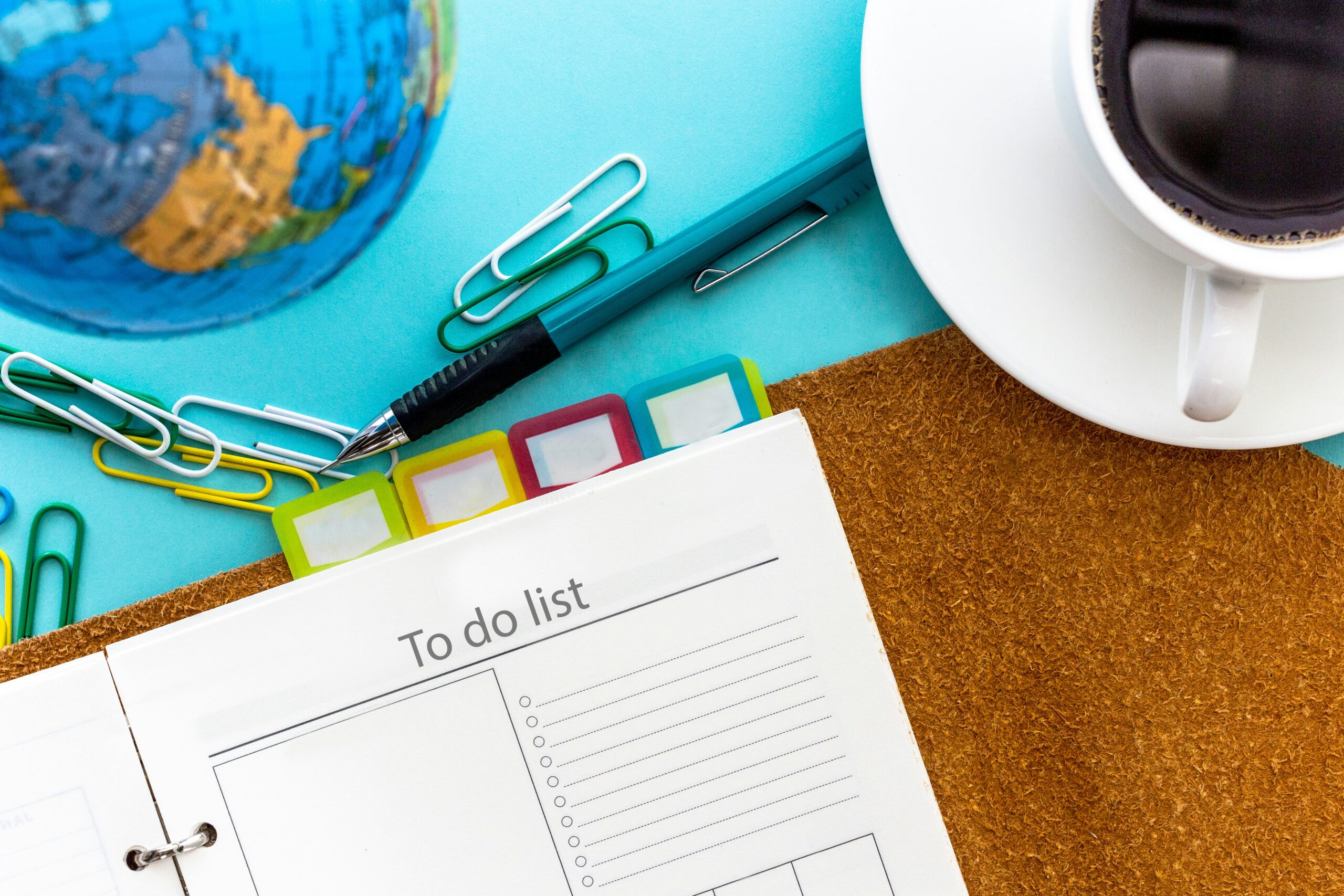 corner of day timer with to-do list title at top of page against blue folder and coffee cup on desk.