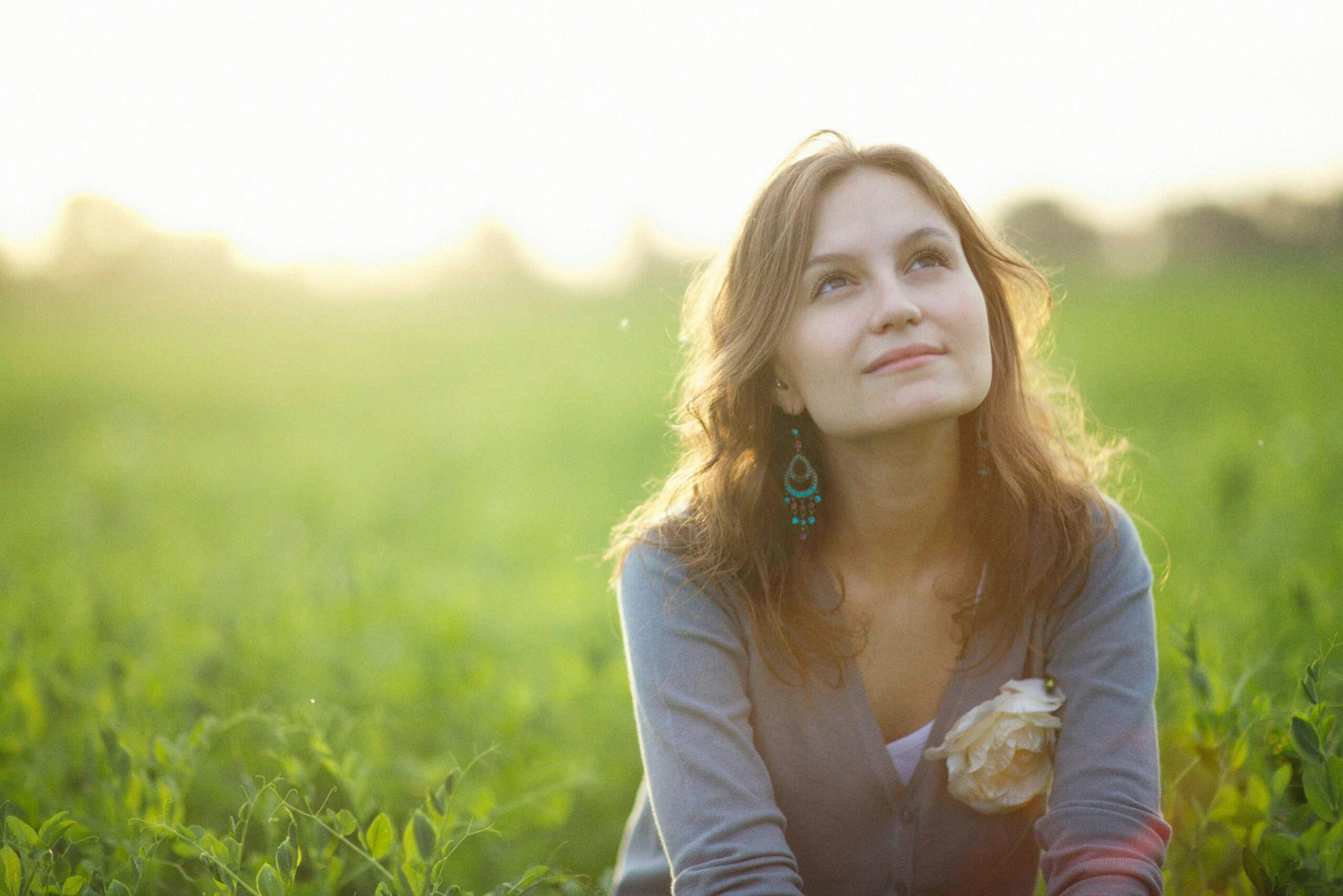 woman sitting in field looking upward as if thoughtful.