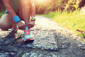 woman on bended knee tying shoe lace on running shoe.